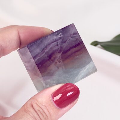 Fluorit regnbue krystal sten kube terning firkant i hånd med hvid baggrund og grønt blad