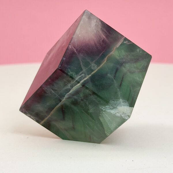 Fluorit regnbue krystal sten kube terning firkant på hvid plade med lyserød baggrund