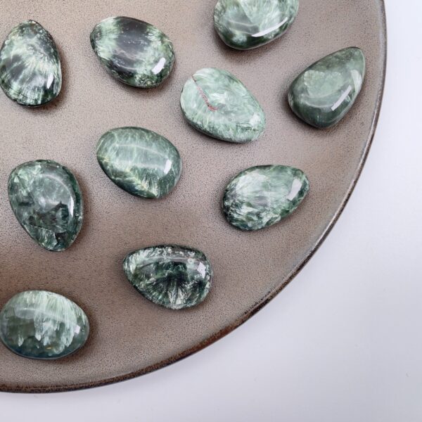 Serafinit håndpoleret krystal lommesten på brunt fad med hvid baggrund