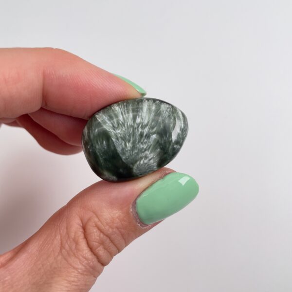 Serafinit håndpoleret krystal lommesten mellem fingre med hvid baggrund