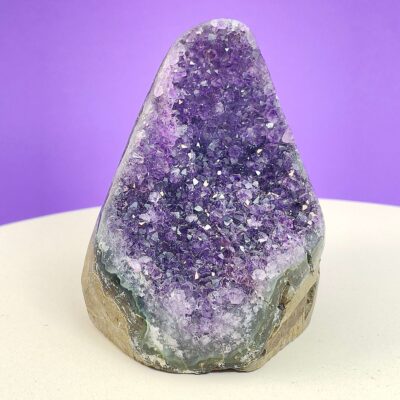 Ametyst krystal rå grotte klynge sten i hånd med hvid baggrund og grønt blad