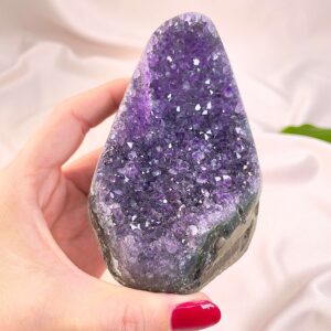 Ametyst krystal rå grotte klynge sten i hånd med hvid baggrund og grønt blad