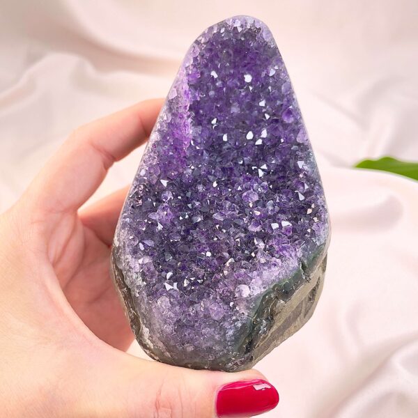 Ametyst krystal rå grotte klynge sten i hånd med hvid baggrund og grønt blad