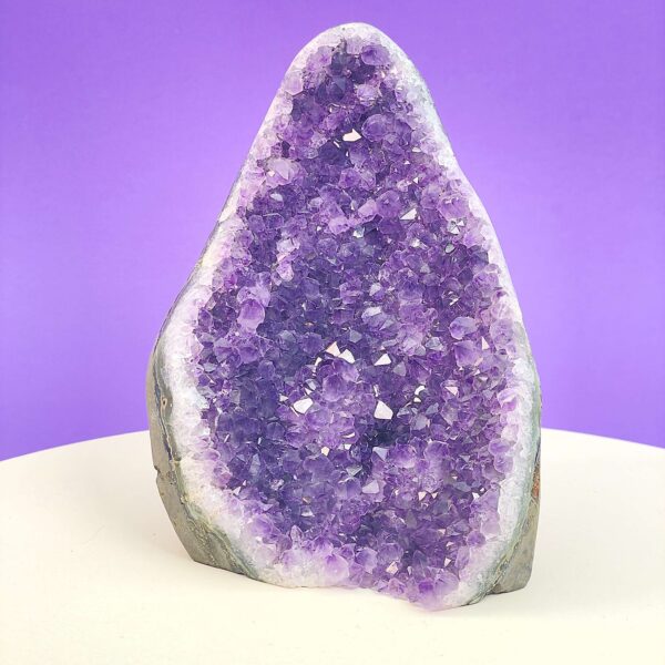 Ametyst krystal rå grotte klynge sten i hånd med hvid baggrund og grønt blad