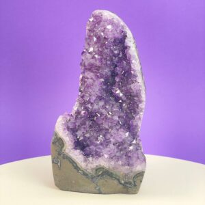 Ametyst krystal rå grotte klynge sten i hånd med hvid baggrund og grønt blad