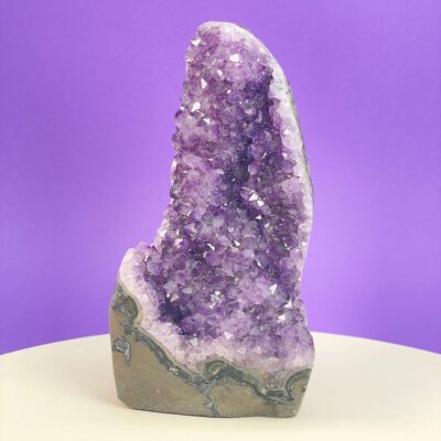 Ametyst krystal rå grotte klynge sten i hånd med hvid baggrund og grønt blad