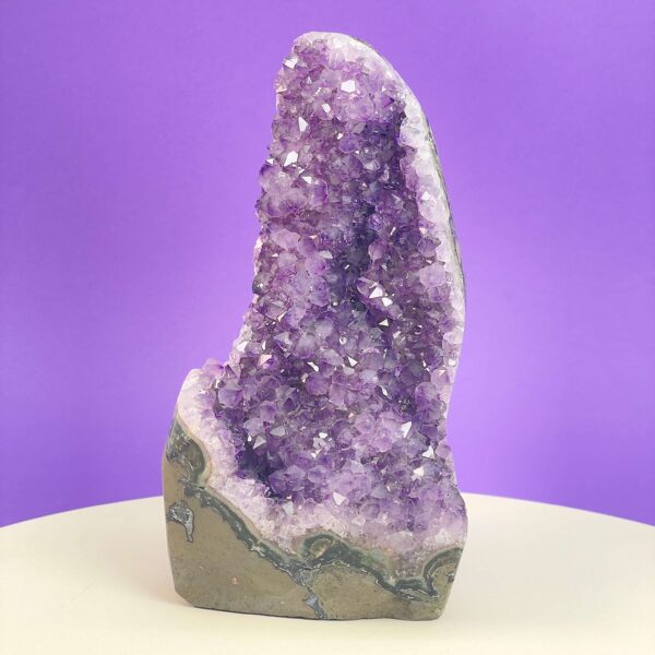 Ametyst krystal rå grotte klynge sten i hånd med hvid baggrund og grønt blad