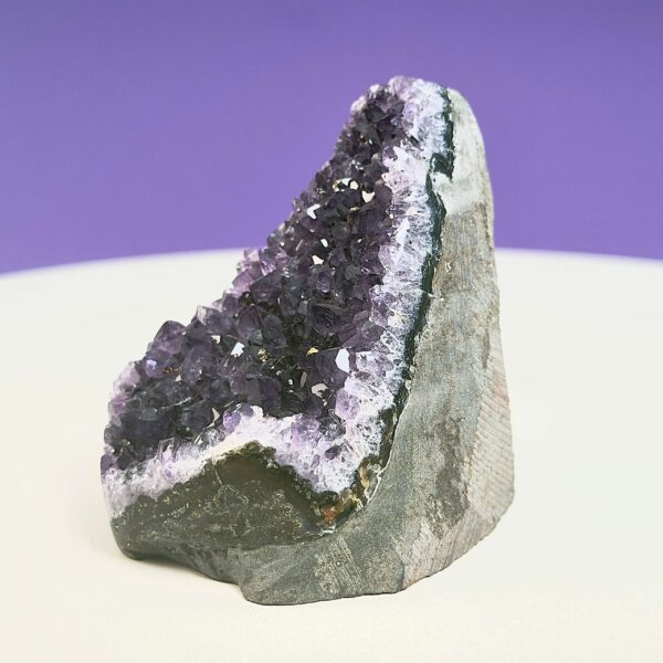 Ametyst krystal rå grotte klynge sten på hvid plade med lilla baggrund fra siden