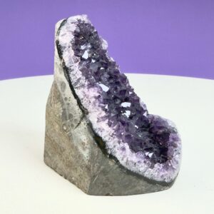Ametyst krystal rå grotte klynge sten på hvid plade med lilla baggrund fra siden