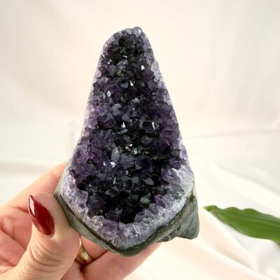 Ametyst krystal rå grotte klynge sten i hånd med hvid baggrund og grønt blad