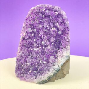 Ametyst krystal rå grotte klynge sten i hånd med hvid baggrund og grønt blad