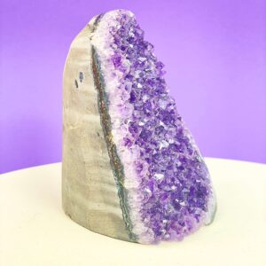 Ametyst krystal rå grotte klynge sten i hånd med hvid baggrund og grønt blad fra siden