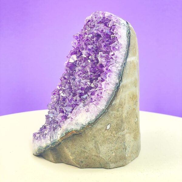 Ametyst krystal rå grotte klynge sten i hånd med hvid baggrund og grønt blad fra siden