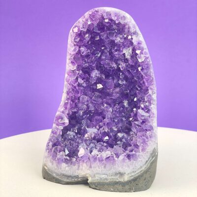 Ametyst krystal rå grotte klynge sten i hånd med hvid baggrund og grønt blad