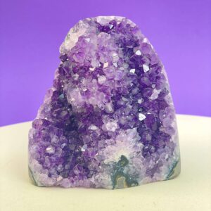 Ametyst krystal rå grotte klynge sten i hånd med hvid baggrund og grønt blad