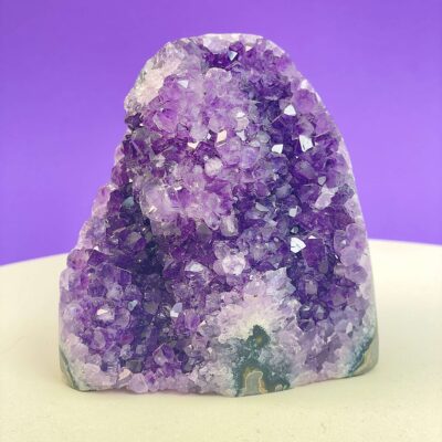 Ametyst krystal rå grotte klynge sten i hånd med hvid baggrund og grønt blad