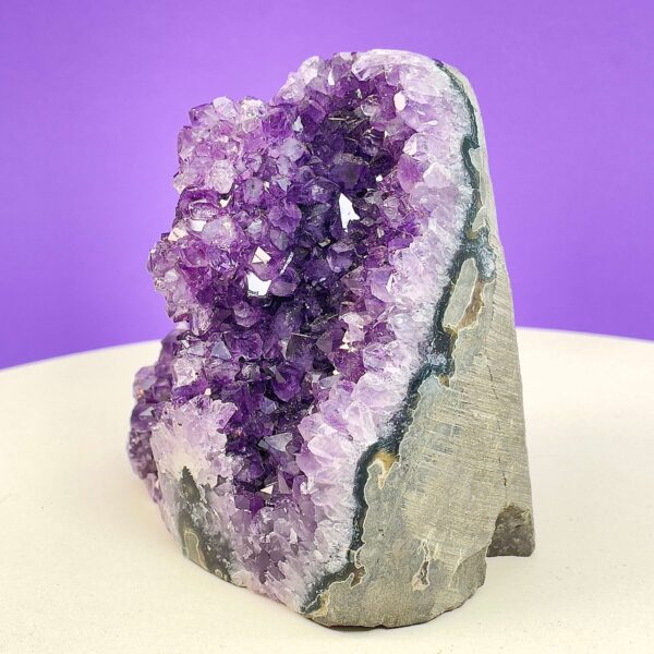 Ametyst krystal rå grotte klynge sten i hånd med hvid baggrund og grønt blad fra siden