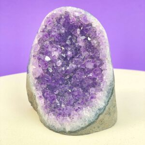 Ametyst krystal rå grotte klynge sten i hånd med hvid baggrund og grønt blad