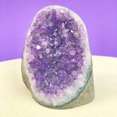 Ametyst krystal rå grotte klynge sten i hånd med hvid baggrund og grønt blad