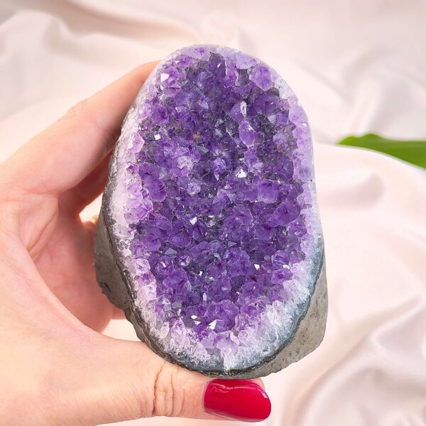 Ametyst krystal rå grotte klynge sten i hånd med hvid baggrund og grønt blad