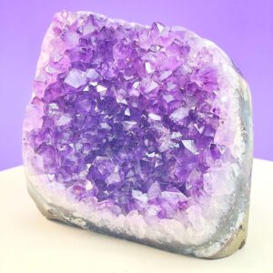 Ametyst krystal rå grotte klynge sten i hånd med hvid baggrund og grønt blad