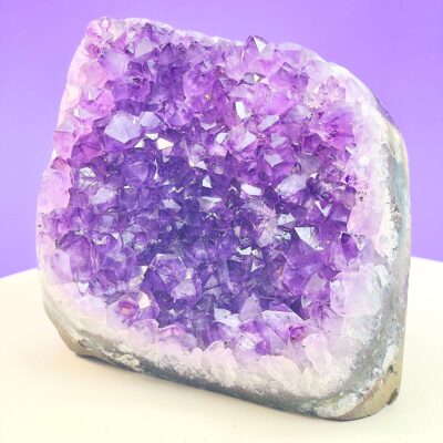 Ametyst krystal rå grotte klynge sten i hånd med hvid baggrund og grønt blad