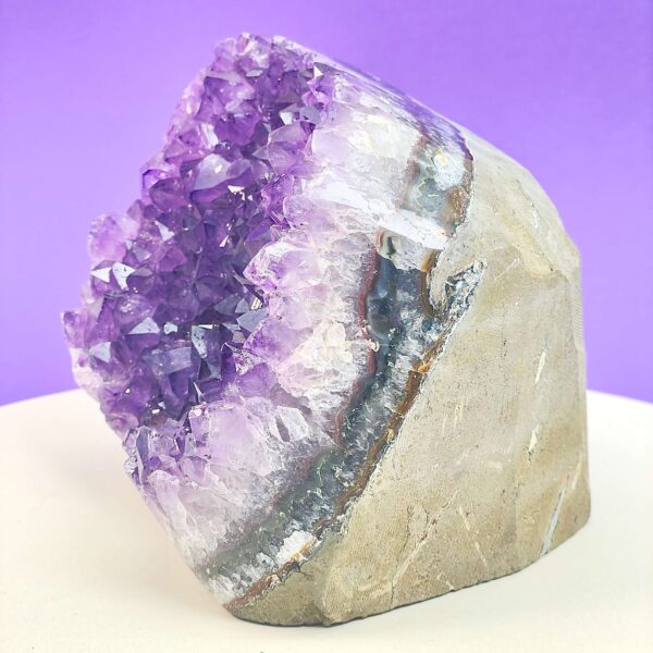 Ametyst krystal rå grotte klynge sten i hånd med hvid baggrund og grønt blad fra siden