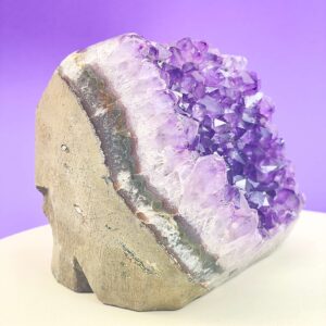 Ametyst krystal rå grotte klynge sten i hånd med hvid baggrund og grønt blad fra siden