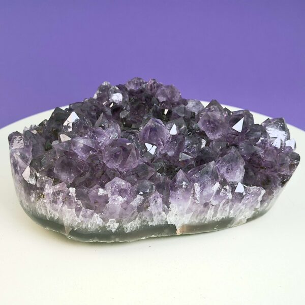 Ametyst krystal rå grotte klynge sten på hvid plade med lilla baggrund skrå