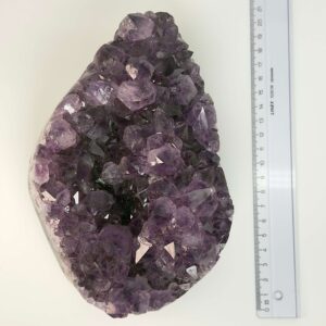 Ametyst krystal rå grotte klynge sten ved siden af lineal på hvid baggrund