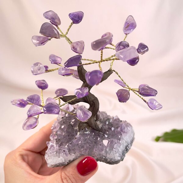 Ametyst træ på krystal bund i hånd med lys baggrund og grønt blad