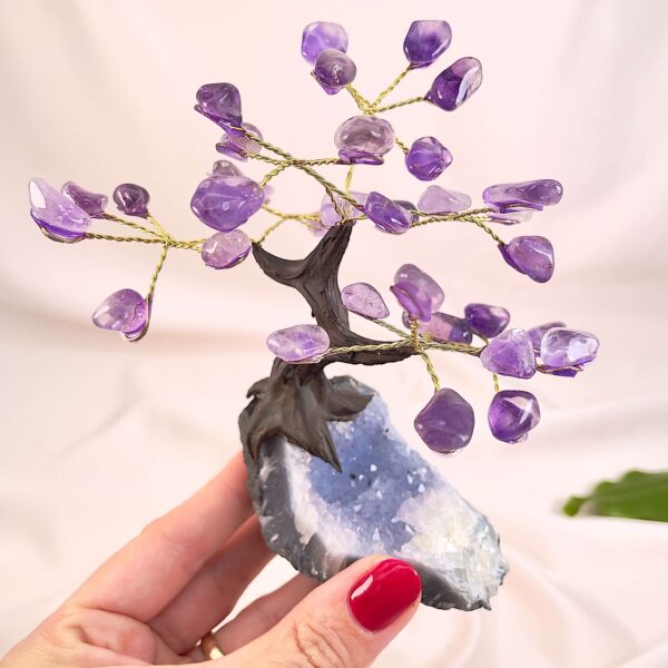 Ametyst træ på krystal bund i hånd med lys baggrund og grønt blad