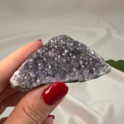 Ametyst krystal rå klynge sten i hånd med hvid baggrund og grønt blad