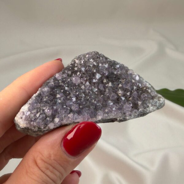 Ametyst krystal rå klynge sten i hånd med hvid baggrund og grønt blad