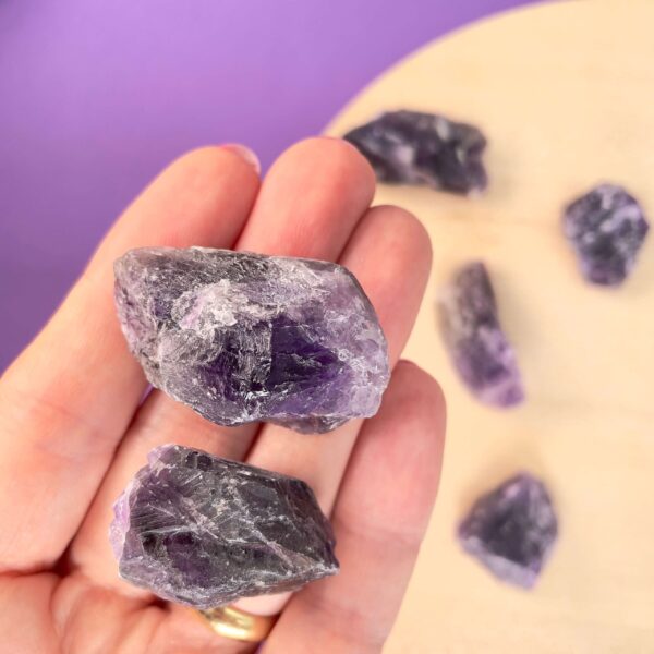 Ametyst rå i hånd med ametyst rå sten på træplade bagved