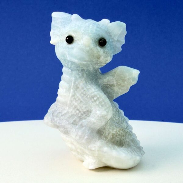 Blå calsit krystal babydrage på hvid plade med blå baggrund