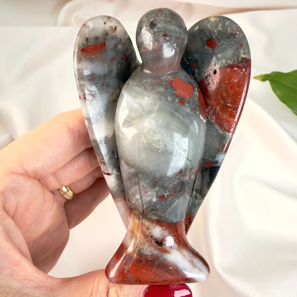 Blodsten krystal engel mellem fingre med hvid baggrund og grønt blad