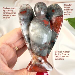 Blodsten krystal engel mellem fingre med hvid baggrund og grønt blad med tags