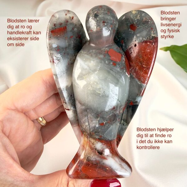 Blodsten krystal engel mellem fingre med hvid baggrund og grønt blad med tags