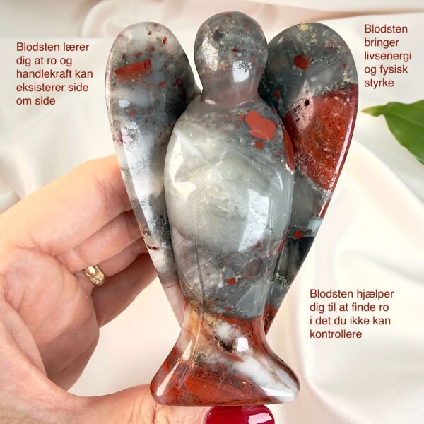 Blodsten krystal engel mellem fingre med hvid baggrund og grønt blad med tags