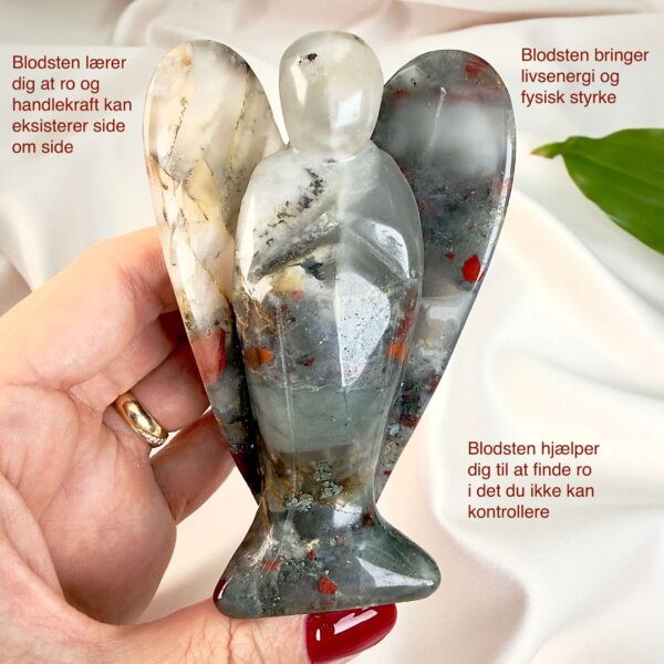 Blodsten krystal engel mellem fingre med hvid baggrund og grønt blad med tags