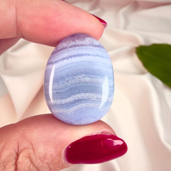 Blondeagat håndpoleret krystal lommesten mellem fingre på hvid baggrund med grønt blad