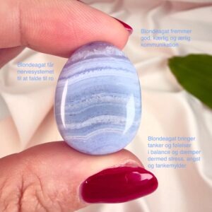 Blondeagat håndpoleret krystal lommesten mellem fingre på hvid baggrund med grønt blad med tags