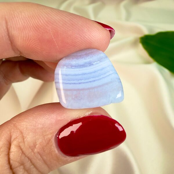 Blondeagat krystal lommesten mellem fingre på hvid baggrund med grønt blad