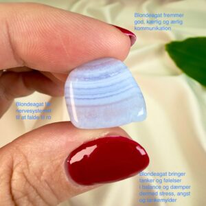 Blondeagat krystal lommesten mellem fingre på hvid baggrund med grønt blad med tags