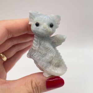 Blå Calsit krystal babydrage på imellem fingre hvid baggrund