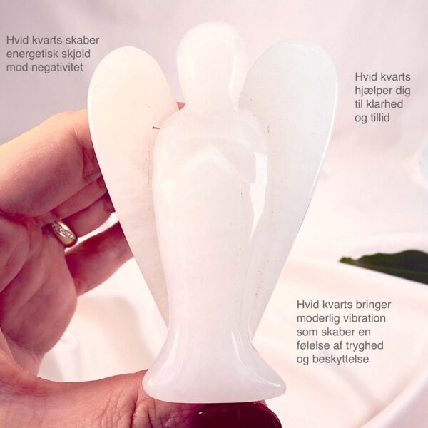 Hvid kvarts krystal engel mellem fingre med hvid baggrund og grønt blad og tags