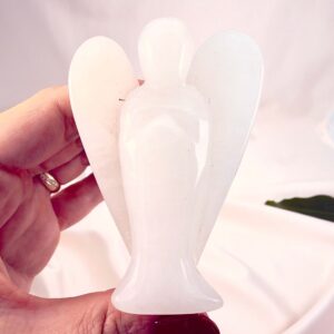 Hvid kvarts krystal engel mellem fingre med hvid baggrund og grønt blad