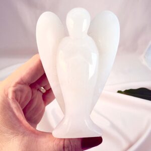 Hvid kvarts 10 cm krystal engel imellem fingre med hvid baggrund og grønt blad