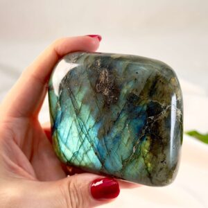 Labradorit krystal freeform støtte mellem fingre på hvid baggrund med grønt blad